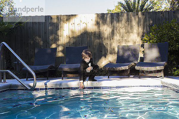 Ein Junge in schwarzem Anzug und Fliege steht an einem Swimmingpool