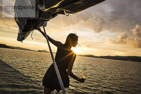 Frau mit Weinglas in der Hand an Bord eines Schiffes  Dinner-Kreuzfahrt bei Sonnenuntergang auf dem Indischen Ozean.