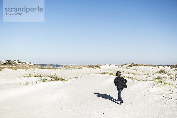 Ein sechsjähriger Junge  der im Freien über Sanddünen läuft.
