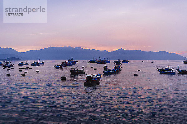Große Gruppe von Fischern in traditionellen Fischerbooten bei Sonnenaufgang auf dem See  Berge in der Ferne.