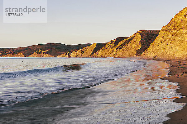 Steile Klippen und Strand mit Brandung in der Morgendämmerung