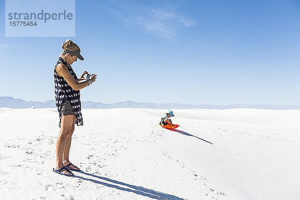 Mutter fotografiert Sohn beim Schlittenfahren auf Sanddünen