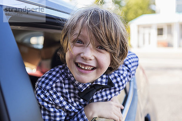 Ein sechsjähriger Junge lächelt in die Kamera und schaut aus dem Autofenster