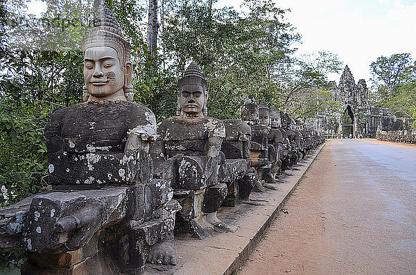 Ankor Wat  ein historischer Khmer-Tempel aus dem 12. Jahrhundert und UNESCO-Weltkulturerbe. Büsten und Statuen von Gottheiten und Wächterfiguren entlang eines Weges zu einer Stupa und einem Eingangsbogen.