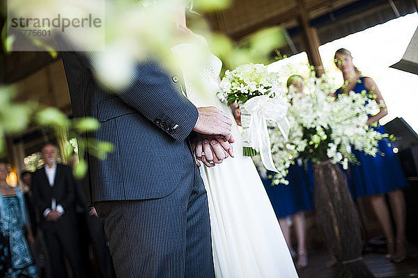 Nahaufnahme von Braut und Bräutigam  die bei einer Hochzeitszeremonie Händchen halten.