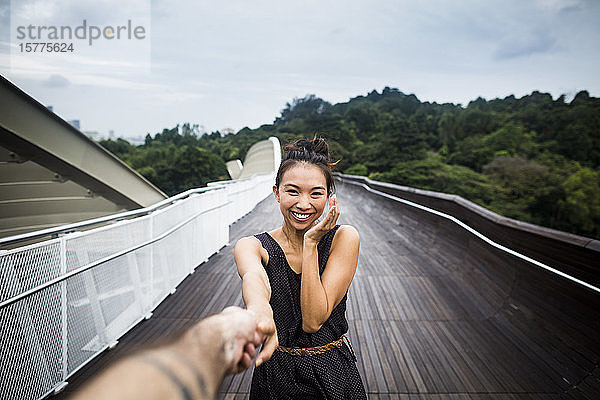 Lächelnde junge Frau  die auf einer Brücke steht und die Hand eines Mannes hält.