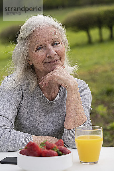Lächelnde ältere Frau im Garten sitzend
