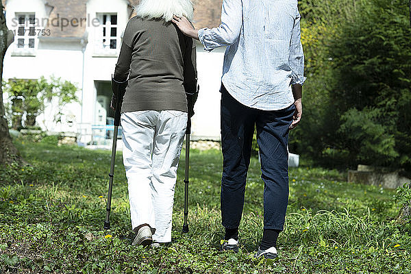 Pflegerin und ältere Frau gehen im Garten spazieren