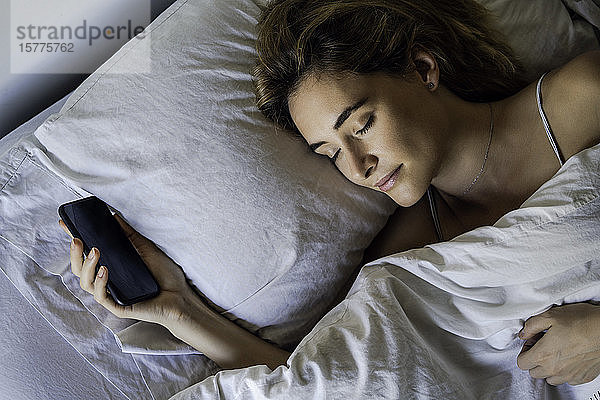 Junge Frau schläft mit Smartphone