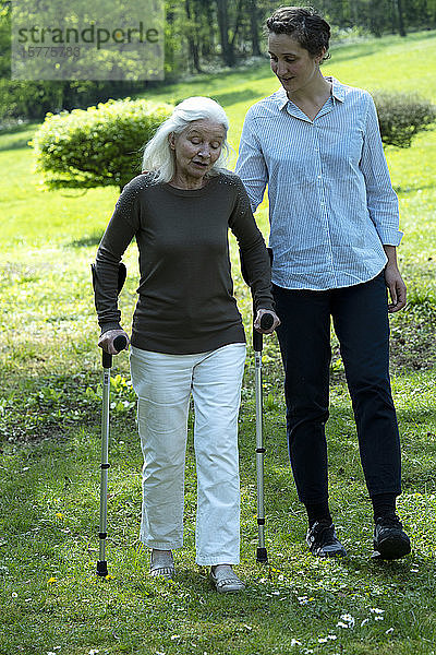 Pflegerin und ältere Frau gehen im Garten spazieren
