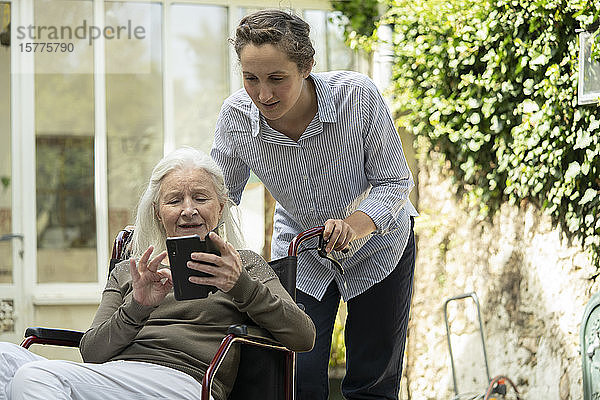 Eine ältere Patientin zeigt einem jungen Pfleger ihr Handy
