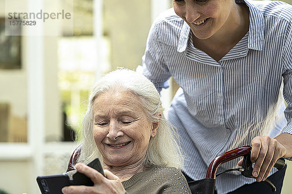 Eine ältere Patientin zeigt einem jungen Pfleger ihr Handy