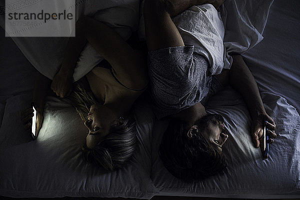 Junges Paar benutzt Smartphones auf dem Bett