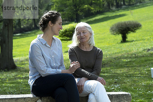 Pflegerin und ältere Frau sitzen im Garten
