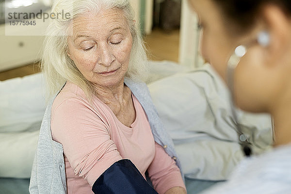 Hauspflegerin prüft Blutdruck einer älteren Frau