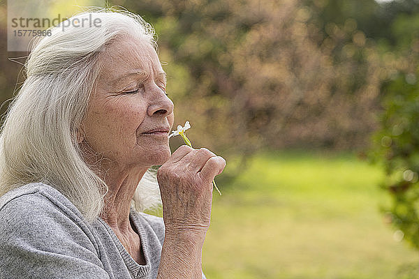 Ältere Frau riecht an einer Blume im Garten
