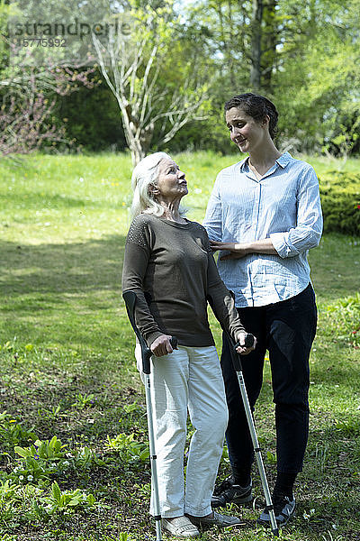 Pflegerin und ältere Frau im Garten stehend