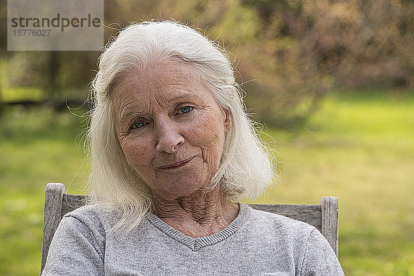 Porträt einer älteren Frau  die im Garten sitzt