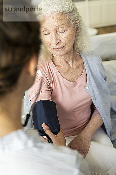 Hauspflegerin prüft Blutdruck einer älteren Frau