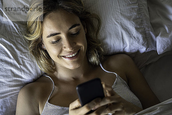Junge Frau benutzt Smartphone auf dem Bett