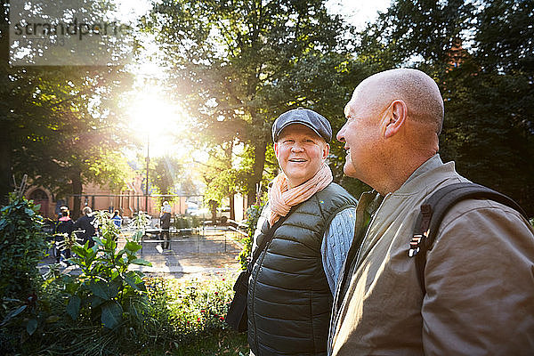 Lächelnder älterer Mann geht mit einem Freund im Park gegen Bäume in der Stadt