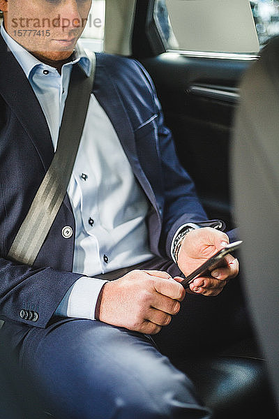 Ein reifer Geschäftsmann benutzt ein Mobiltelefon  während er im Auto sitzt