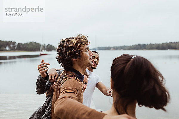 Lächelnde Freunde mit Armen um sich herum  die im Urlaub am Meer gegen den Himmel stehen