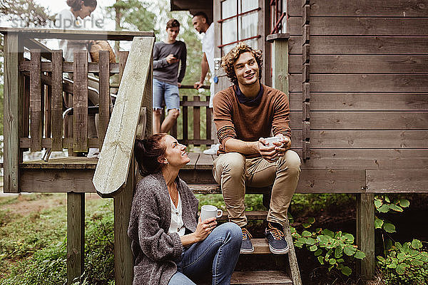 Lächelnde Frau schaut Mann an  der auf Stufen sitzt  während Freunde im Hintergrund stehen