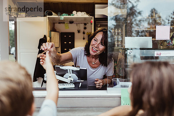 Lächelnde Besitzerin gibt Löffel an Kunden ab  die an einem Konzessionsstand stehen