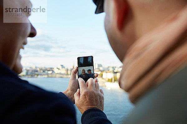 Homosexuelles Paar  das sich mit seinem Handy gegen den Himmel in der Stadt wendet