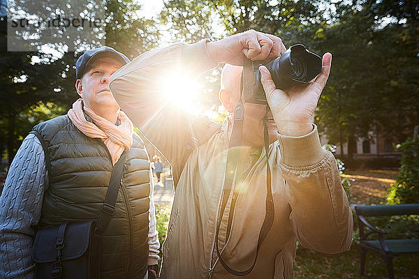 Älterer Mann benutzt Digitalkamera  während er mit einem Freund im Park in der Stadt steht