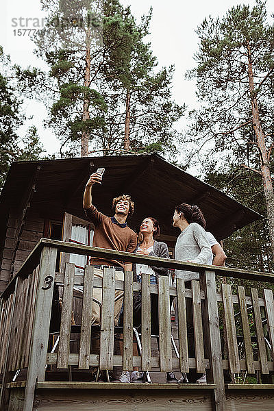 Lächelnde Freunde  die auf der Veranda stehen und sich mit dem Handy selbstständig machen