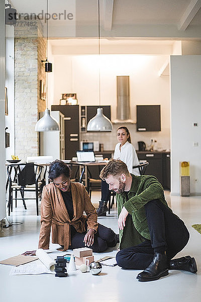 Lächelnde Architekten arbeiten  während eine Unternehmerin im Hintergrund im Home-Office sitzt