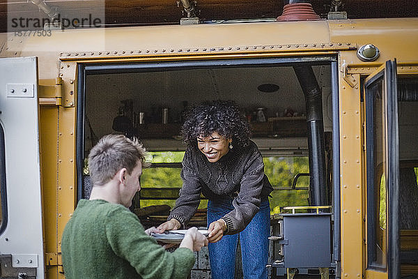 Lächelnde Frau schaut  während sie beim Camping mit einem Freund den Teller hält