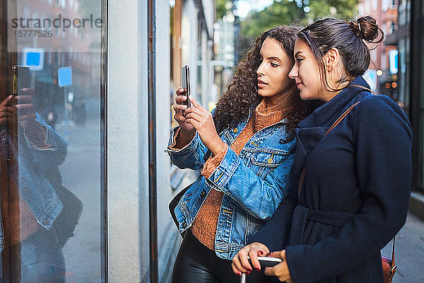 Freundinnen fotografieren Schaufenster mit Smartphone in der Stadt