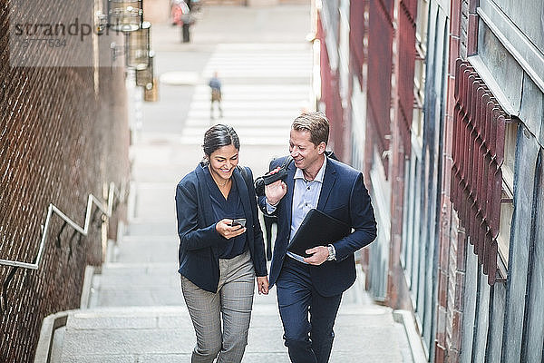 Lächelnde Unternehmer und Unternehmerinnen  die beim Treppensteigen in der Stadt telefonieren