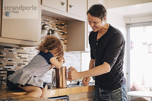 Glücklicher Vater sieht Tochter an  die französische Presse schiebt  während er auf der Küchentheke sitzt