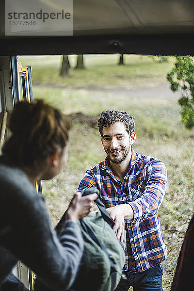 Lächelnder Mann nimmt Gepäck von Frau beim Entladen des Wohnwagens beim Camping