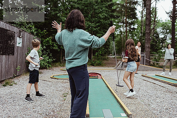 Rückansicht einer Frau  die mit ihrer Familie im Garten Minigolf spielt