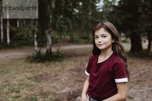 Porträt eines lächelnden Mädchens  das bei Bäumen im Wald steht