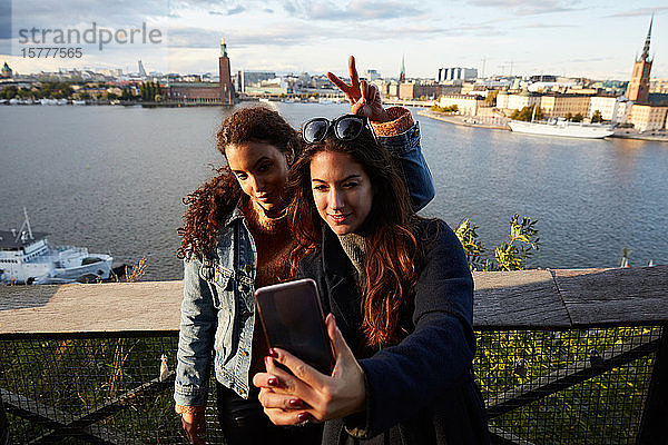 Lesbisches Paar  das sich mit dem Handy gegen ein Geländer am Stadtbild wendet