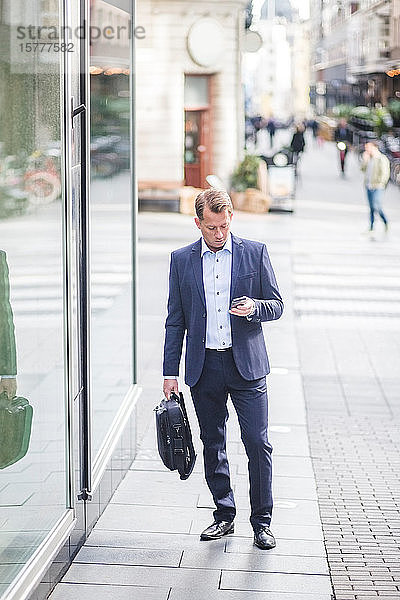 Ein reifer Geschäftsmann benutzt ein Smartphone  während er in der Stadt steht