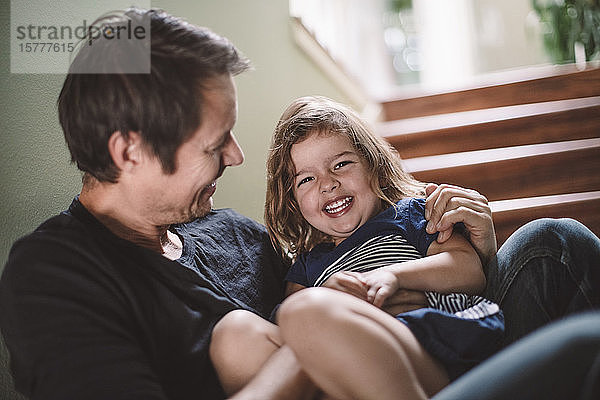 Porträt einer glücklichen Tochter mit lächelndem Vater  der zu Hause auf den Stufen sitzt