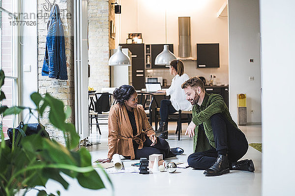 Lächelnde Architekten diskutieren  während eine Unternehmerin im Hintergrund im Home-Office arbeitet
