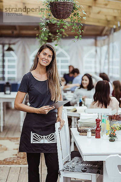 Porträt einer lächelnden Besitzerin  die ein digitales Tablet hält und im Restaurant steht