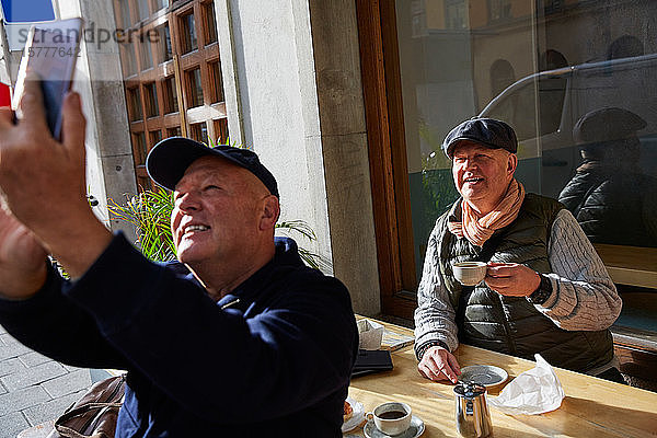 Lächelndes schwules Pärchen  das sich mit dem Handy selbstständig macht  während es im Straßencafé sitzt