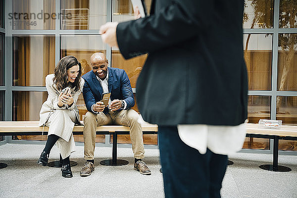 Glückliche Unternehmer und Unternehmerinnen telefonieren  während sie vor einem Bürogebäude sitzen