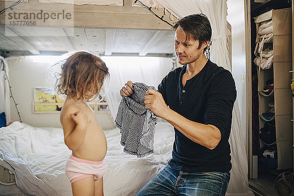 Vater kleidet Tochter im Schlafzimmer an