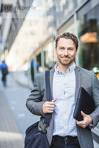 Porträt eines lächelnden reifen Unternehmers mit im Freien stehender Tasche