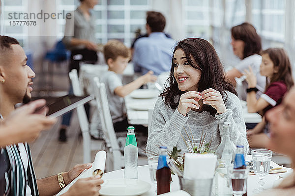 Lächelnde Frau unterhält sich mit einem männlichen Freund  während sie im Restaurant sitzt